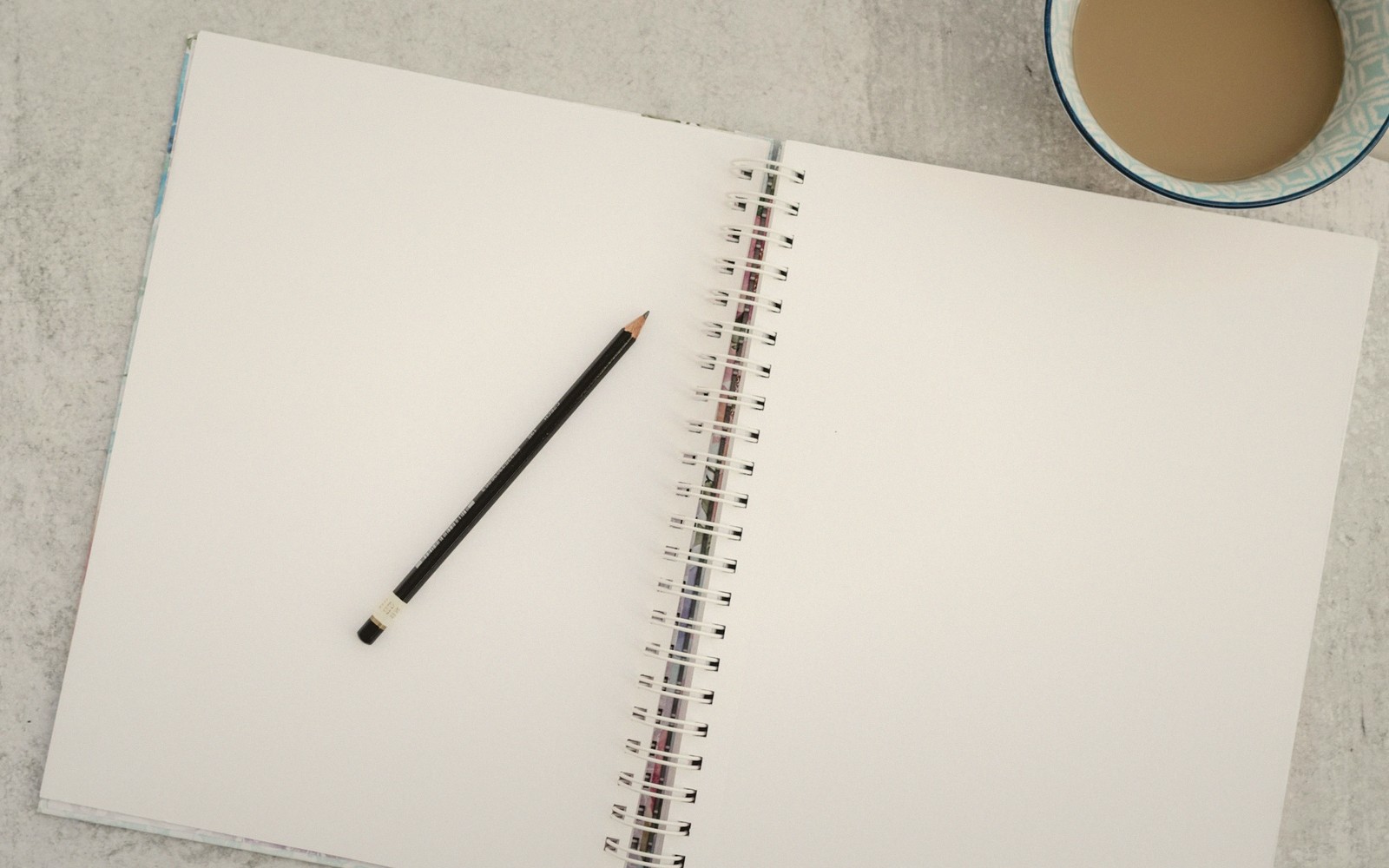 a pencil resting on an open notebook beside a cup